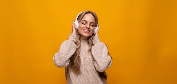 cute lady joyfully listens to music with big headphones on orange background.