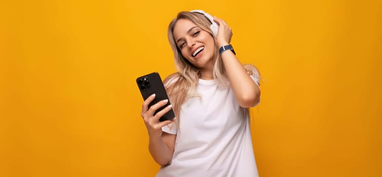 a girl listens to music in headphones with a connected phone on a yellow background.