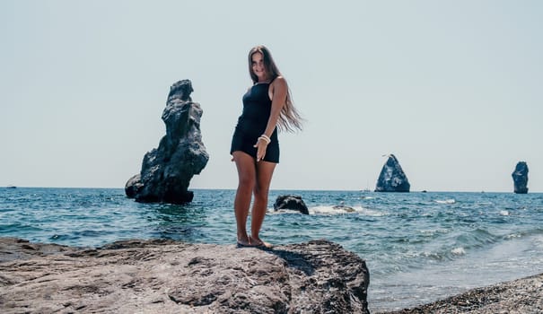 Woman travel sea. Young Happy woman in a long red dress posing on a beach near the sea on background of volcanic rocks, like in Iceland, sharing travel adventure journey