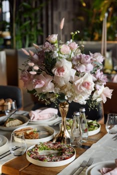 served table in the restaurant is decorated with a luxurious bouquet. Garden roses, eustoma, populus eucalyptus. pastel colours.