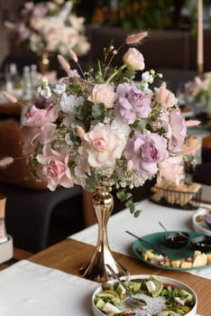 served table in the restaurant is decorated with a luxurious bouquet. Garden roses, eustoma, populus eucalyptus. pastel colours.