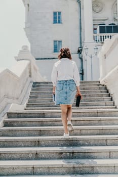 Woman staircase city. A business woman in a white shirt and denim skirt walks down the steps of an ancient building in the city.