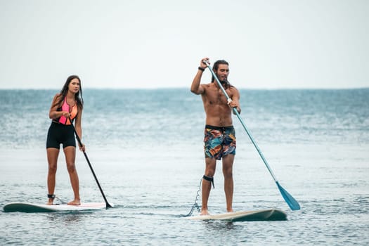 Sea woman and man on sup. Silhouette of happy young woman and man, surfing on SUP board, confident paddling through water surface. Idyllic sunset. Active lifestyle at sea or river