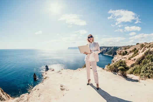 Digital nomad, Business woman working on laptop by the sea. Pretty lady typing on computer by the sea at sunset, makes a business transaction online from a distance. Freelance remote work on vacation