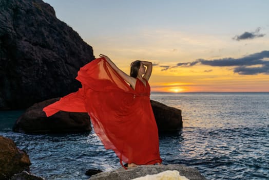 Woman in a red flying dress on the ocean or on the sea beach against the backdrop of the sunset sky
