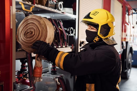 Holds hose. Male firefighter in protective uniform standing near truck.