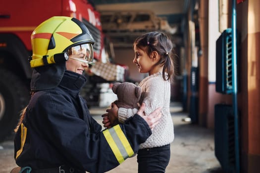 Happy little girl is with female firefighter in protective uniform.