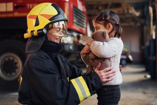 Happy little girl is with female firefighter in protective uniform.