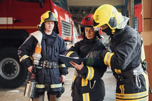 With notepad. Group of firefighters in protective uniform that is on station.