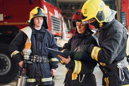 With notepad. Group of firefighters in protective uniform that is on station.