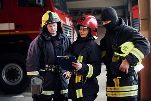 With notepad. Group of firefighters in protective uniform that is on station.