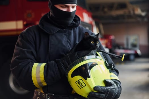 Portrait of firefighter in protective uniform that holds cute little black cat.