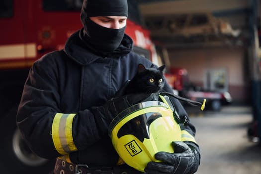 Portrait of firefighter in protective uniform that holds cute little black cat.