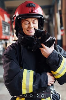 Cute black cat. Female firefighter in protective uniform standing near truck.