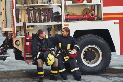 Male and female firefighters in protective uniform is outdoors together.