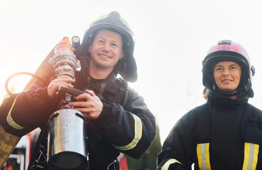 Male and female firefighters in protective uniform is outdoors together.