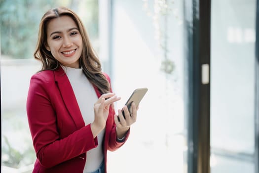 Portrait of beautiful young businesswoman standing smiling and using smartphone.