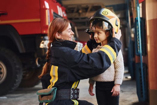 Happy little girl is with female firefighter in protective uniform.