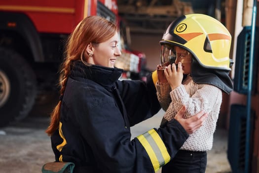 Happy little girl is with female firefighter in protective uniform.