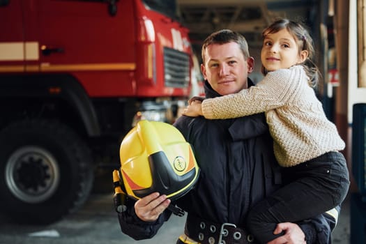 Happy little girl is with male firefighter in protective uniform.