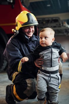 Cute little boy is with male firefighter in protective uniform.