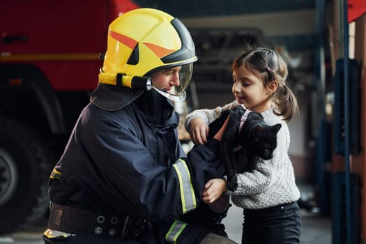 Cute black cat. Happy little girl is with male firefighter in protective uniform.