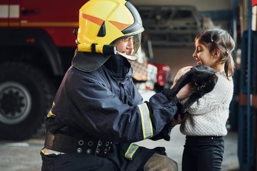Cute black cat. Happy little girl is with male firefighter in protective uniform.