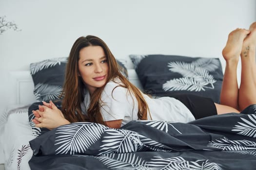 Front view of happy relaxed woman on bed. Interior and design of beautiful modern bedroom at daytime.