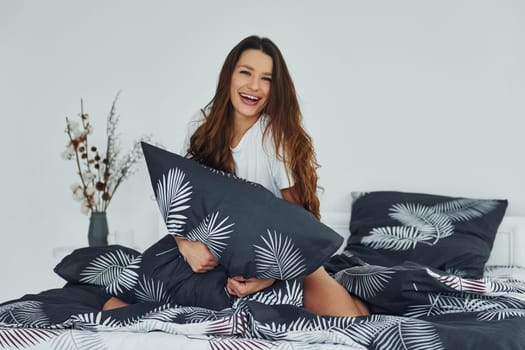 Front view of happy relaxed woman on bed. Interior and design of beautiful modern bedroom at daytime.