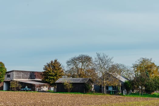 Rural farm in autumn season. Farm in autumn season. Countryside farm house. Farm in autumn scene. Rural scene with houses at the field under cloudy sky in `October. Field in first plan