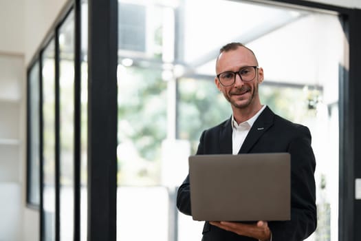 businessman handsome smiling using laptop while standing in office.