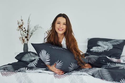 Front view of happy relaxed woman on bed. Interior and design of beautiful modern bedroom at daytime.