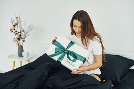 Gift box in hands of young woman. Interior and design of beautiful modern bedroom at daytime.