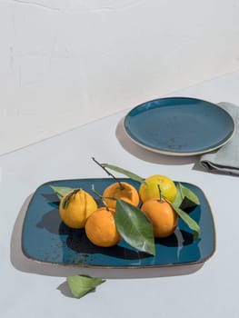 Blue rectangular plate of sweet tangerines with leaves on table next to plate