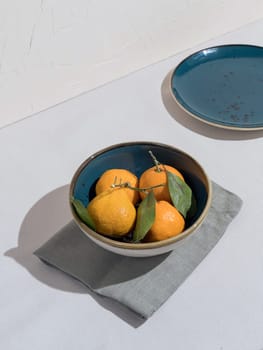 Blue bowl of orange tangerines on table with tablecloth next to plate. Place for your copy