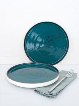 Two empty blue dinner plates with tablecloth on table with white background. Two blue handmade ceramic plates with fork on tablecloth