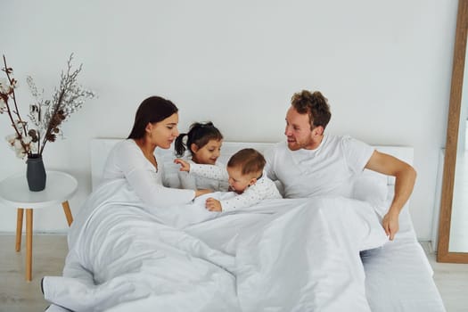 Woman and man lying down on bed with their children. Interior and design of beautiful modern bedroom at daytime.
