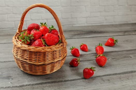 Basket with strawberries, some of them spilled on gray wood desk.