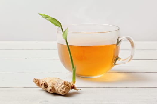 Glass of freshly brewed tea, dry ginger root with green sprout next to it.