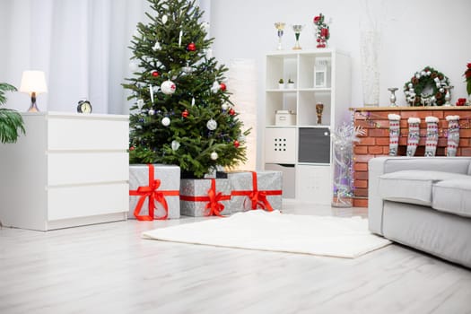 Bright living room with Christams tree and elegant decorations. Elegant gifts with red ribbons and silver paper under the tree