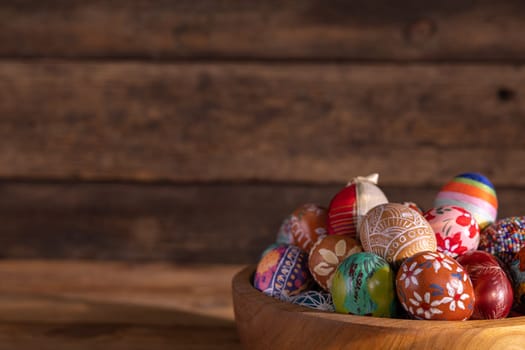 Easter eggs of different colors and patterns were arranged in a wooden bowl. A traditional composition for Easter on a background of boards.