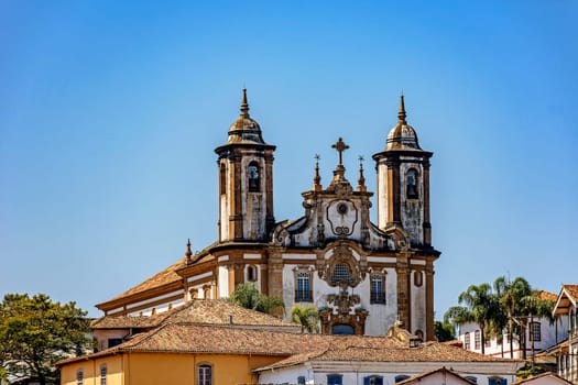 Baroque style historic church tower emerging from behind old houses in Ouro Preto city in Minas Gerais state, Brazil