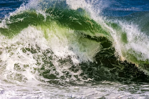 Beautiful and strong sea waves with water drops and foam splashing in the air on a sunny day