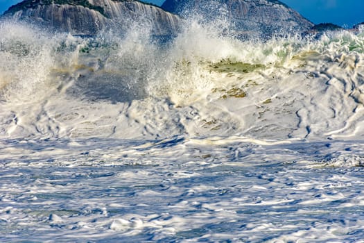 Beautiful and strong sea wave on the beach with water drops and foam splashing in the air on a sunny day