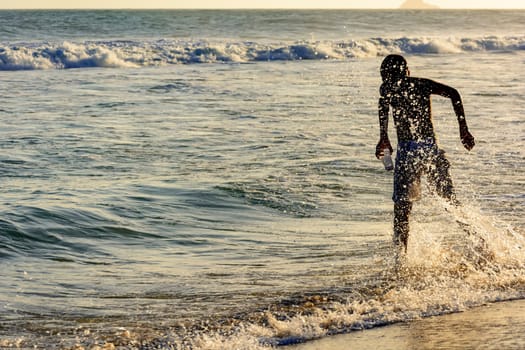 Boy playing with water at the seashore during the summer sunset at Ipanema beach in Rio de Janeiro