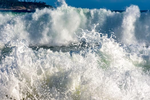 Colorful sea waves crashing on the beach on a sunny summer day with water drops and foam splashing in the air