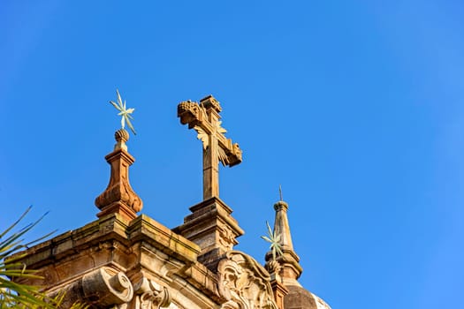 Crucifix and ornaments on top of the facade of an old and historic baroque church in the city of Ouro Preto in Minas Gerais