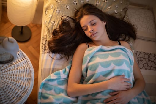 A girl with long hair sleeps peacefully on her bed. A girl under a soft blanket.