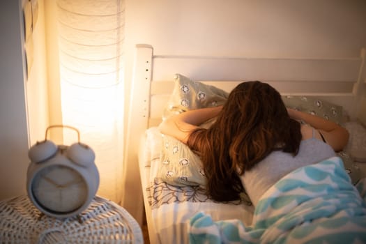 The alarm clock stands on the cabinet next to the bed in which the woman sleeps with the bedside lamp lit. It is already 10 minutes past 10 o'clock on the clock.