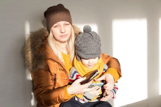 A mother with a small child in her arms is warmly dressed in outerwear, counting money in her purse. The concept of the economic crisis and large utility bills in homes